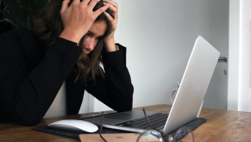 Bild på kvinna med huvudet i händerna framför en datorskärm.